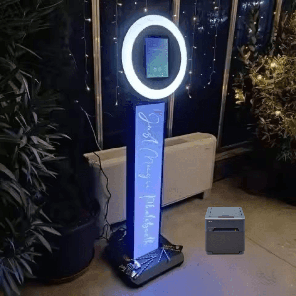 Illuminated photo booth with a glowing ring light in a dimly lit room with plants.