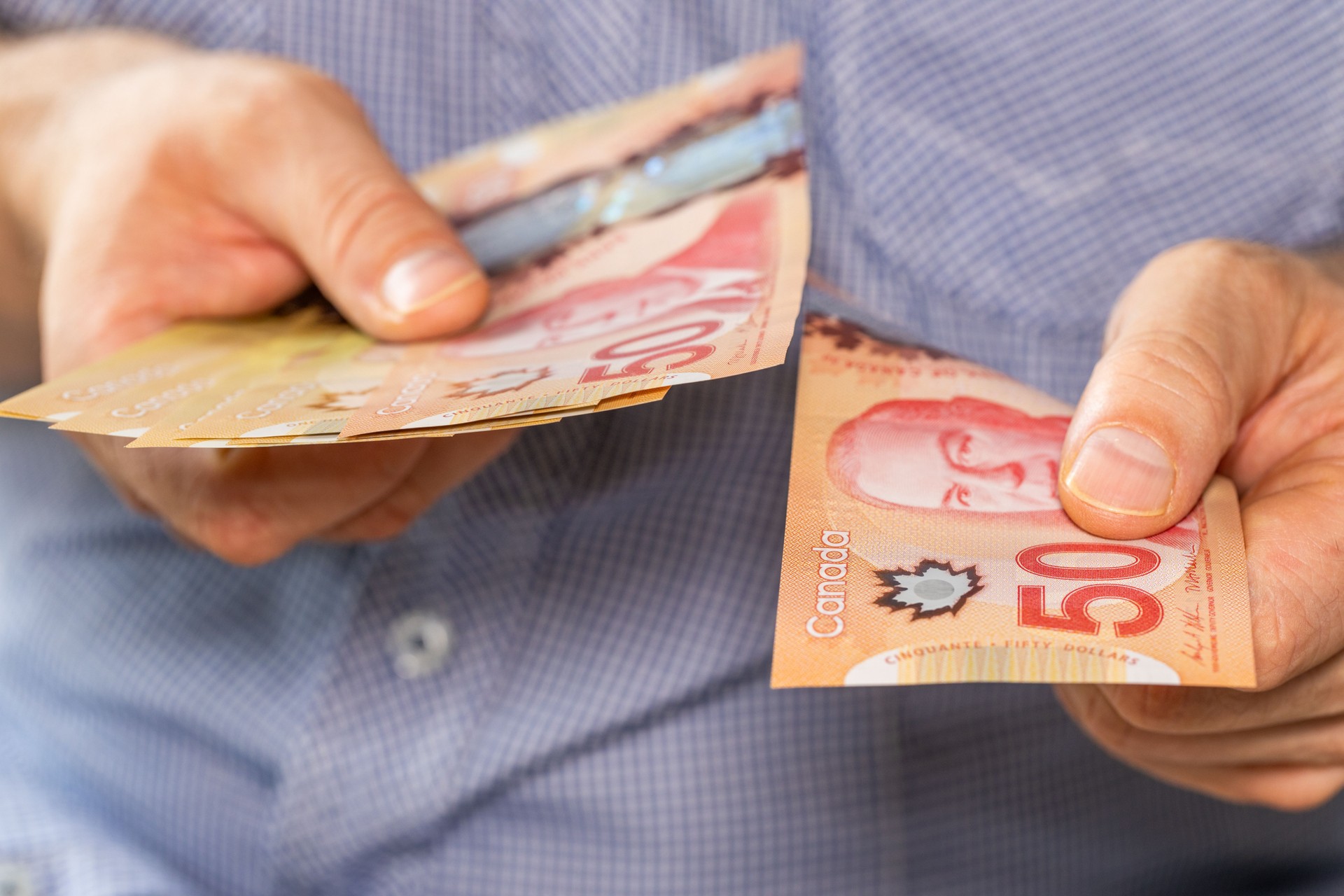 Kanadisches Geld, Mann hält ein Bündel kanadischer Dollar in der Hand und gibt in der anderen Hand einen 50-Dollar-Schein. Geschäfts- und Finanzkonzept